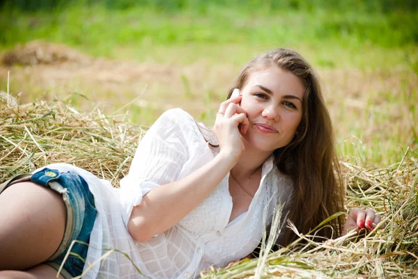 Joven hermosa mujer acostada en el heno un día de verano hablando en el teléfono celular móvil — Foto de Stock