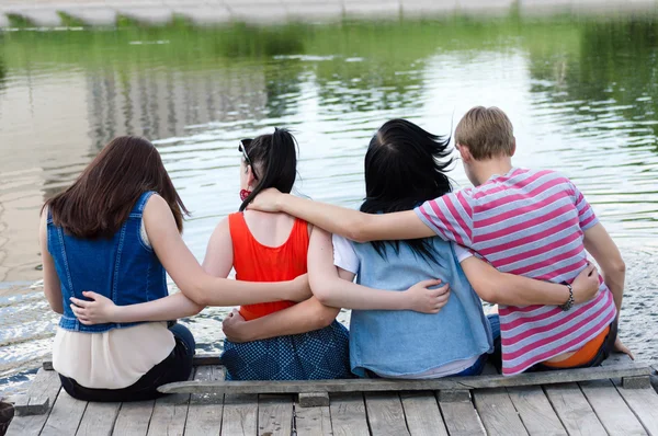 Adolescentes amigos sentados na ponte no rio — Fotografia de Stock