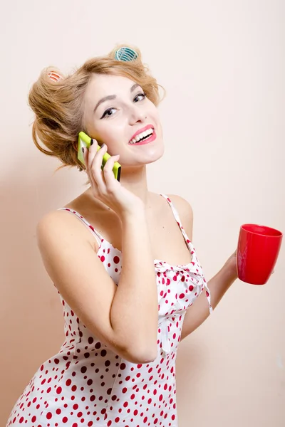 Porträt der schönen blonden, lustigen Pinup-Frau mit grünen Augen & Lockenwicklern, die auf ihrem Handy glücklich lächelnd in die Kamera schaut — Stockfoto