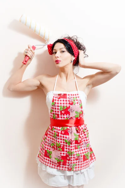 Housewifely young brunette with blue eyes pinup woman with bolster standing near the wall & looking at camera — Stock Photo, Image