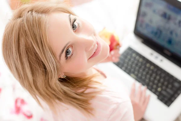 Chica en la cama con ordenador portátil y manzana — Foto de Stock