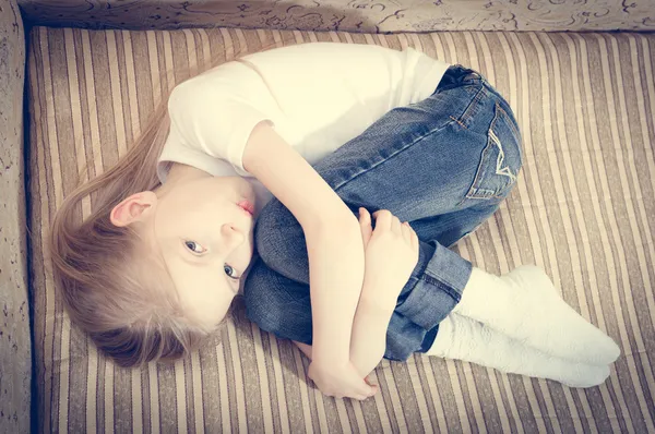 Girl lying on the sofa hugging knees — Stock Photo, Image