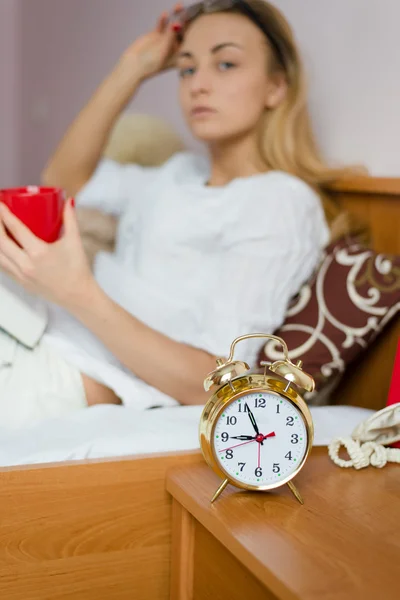 Mulher na cama com copo vermelho e despertador — Fotografia de Stock