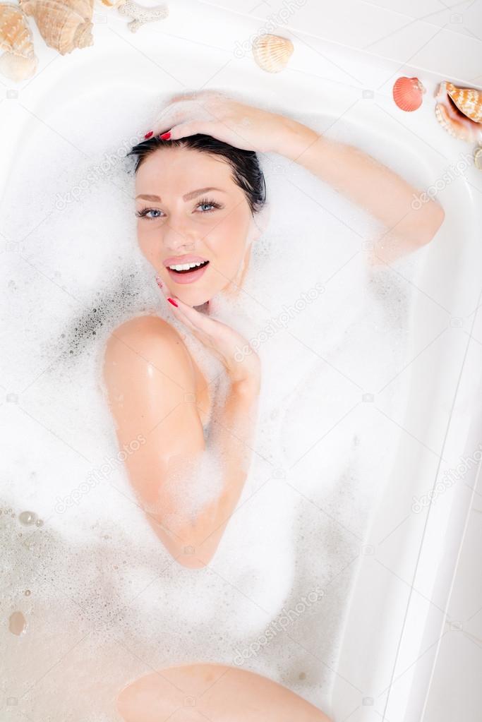Beautiful sexual young woman lying in the bath with foam,smiling & looking at camera
