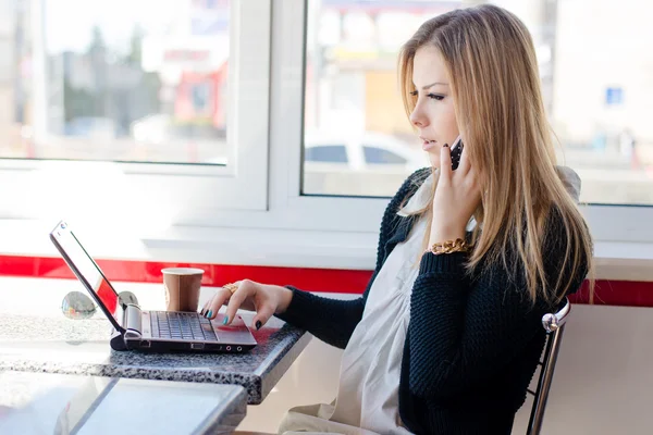 Mulher falando ao telefone trabalhando em um laptop — Fotografia de Stock