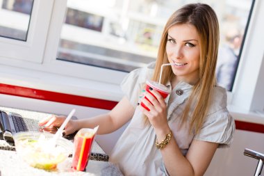 milkshake kokteyl ve çalışma dizüstü bilgisayarda yazarak içme portre portre eğleniyor yeşil gözlü güzel neşeli sarışın genç kadın gülümseyerek ve kamera görüntüsüne bakarak mutlu rahatlatıcı