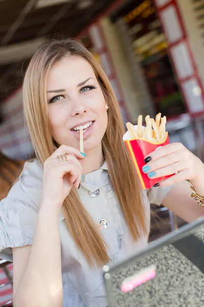 Closeup portrait on eating french fries in fast food coffee shop or restaurant beautiful blond young woman with green eyes having fun relaxing happy smiling & looking into the camera — Stock Photo, Image