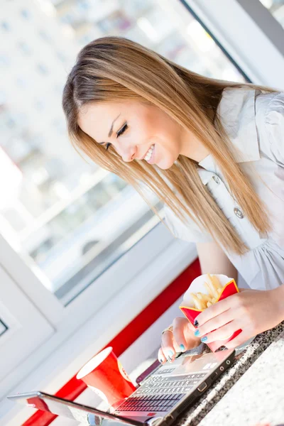 Szybkie działanie diety: zabawy, pisanie na komputerze przenośnym laptopie & jedzenia frytek szczupły piękne zabawne blond dziewczynka szczęśliwy uśmiechający się portret na obraz tła kawiarni lub restauracji — Zdjęcie stockowe