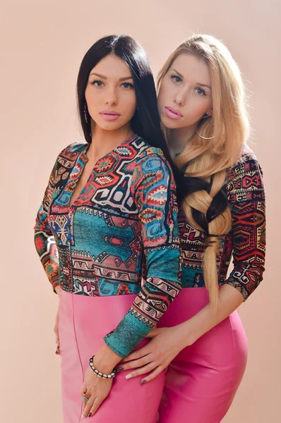 2 belles blondes et brunes sexy jeunes femmes filles amies ou sœurs s'amuser debout ensemble dans des robes en cuir rose regardant la caméra sur fond ivoire portrait — Photo