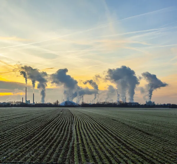 Chimneys and smoke of industry plant with fields in sunrise Stock Picture