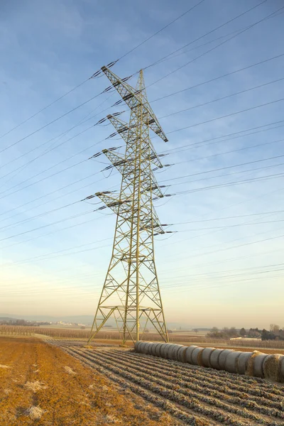 Torre eléctrica en paisaje rural con paca de paja — Foto de Stock