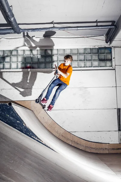 Menino se diverte montando sua scooter no salão de skate — Fotografia de Stock