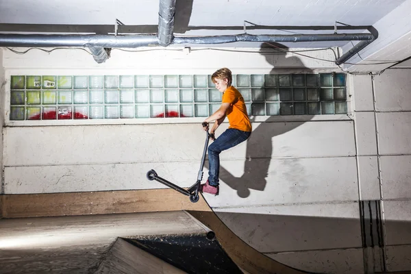 Garçon s'amuse à monter son scooter dans le hall de patinage — Photo