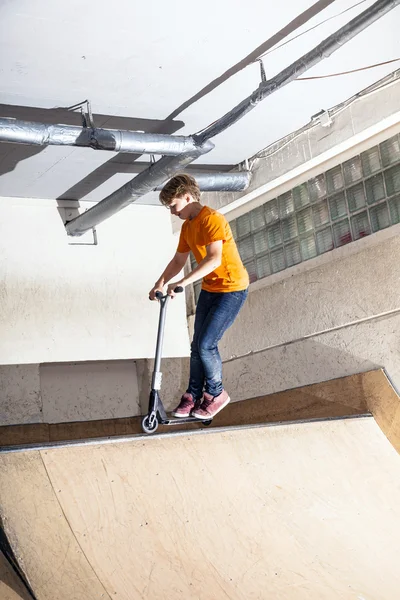 Ragazzo si diverte cavalcando il suo scooter nella sala skate — Foto Stock