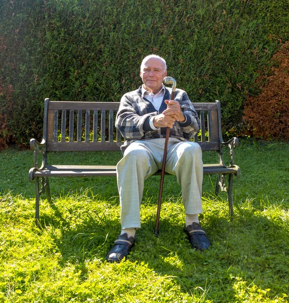 Old man enjoys sitting on a bench in his garden — Stock Photo, Image