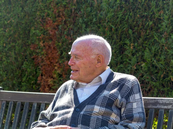 Old man enjoys sitting on a bench in his garden — Stock Photo, Image