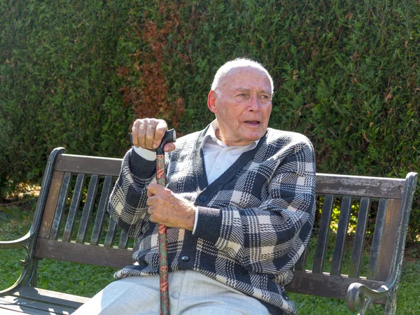 Velho gosta de se sentar em um banco em seu jardim — Fotografia de Stock