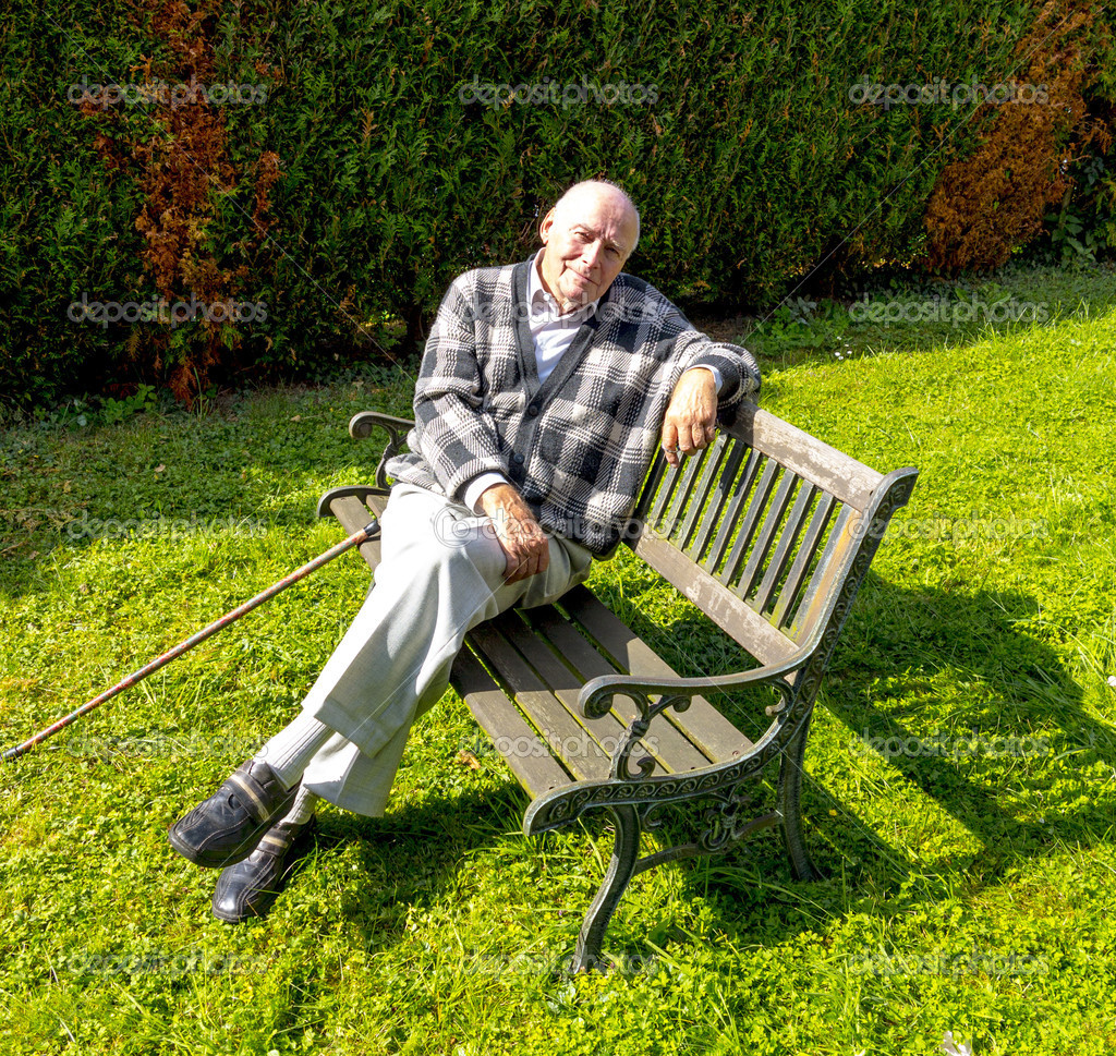 Старий користується, сидячи на лавці в своєму саду 
