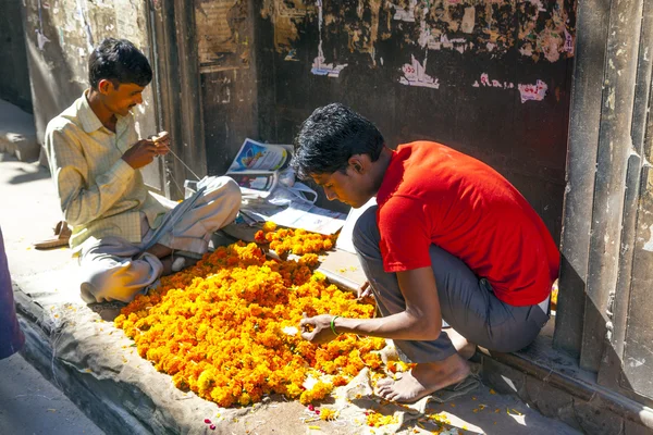 Hombre enhebrando coloridas guirnaldas de flores — Foto de Stock