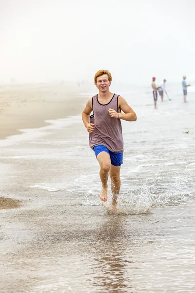 Bonito jovem adolescente menino correndo na praia vazia na parte da manhã — Fotografia de Stock