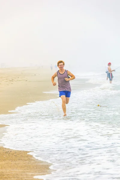 Cute young teenage boy joging at the empty beach in the morning — Stock Photo, Image