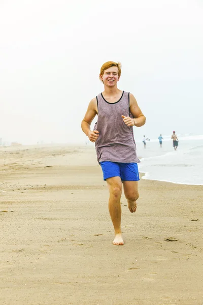 Bonito jovem adolescente menino correndo na praia vazia na parte da manhã — Fotografia de Stock