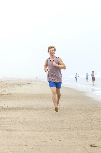 Bonito jovem adolescente menino correndo na praia vazia na parte da manhã — Fotografia de Stock