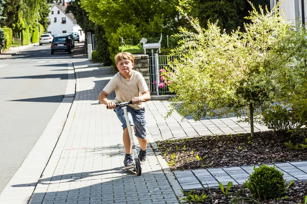 Boy rides his scooter at the sidewalk — Stock Photo, Image