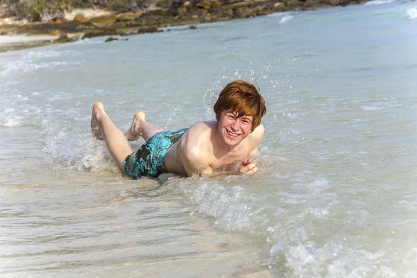 少年を楽しんで、熱帯のビーチの泡立つで横になっています。 — ストック写真