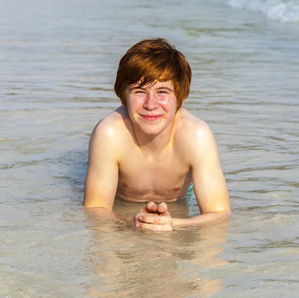 Boy enjoys lying in the spume of the tropical beach Royalty Free Stock Images