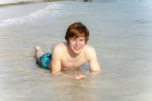 Boy enjoys lying in the spume of the tropical beach Royalty Free Stock Photos