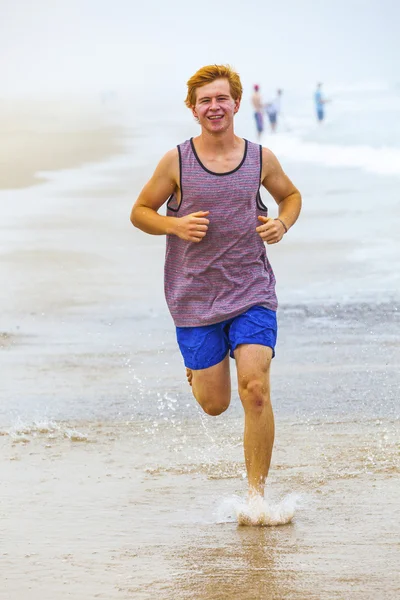 Привлекательный мальчик бегает по пляжу утром — стоковое фото