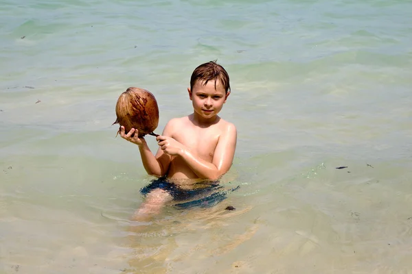 A fiú egy kókuszdióval játszik egy gyönyörű strandon. — Stock Fotó