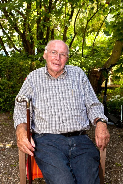 Oudere man zit in een stoel in zijn tuin en ziet er zeer frie — Stockfoto