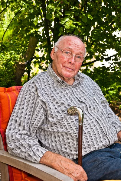 Uomo anziano seduto nel suo giardino e guardando felice e fiducioso — Foto Stock