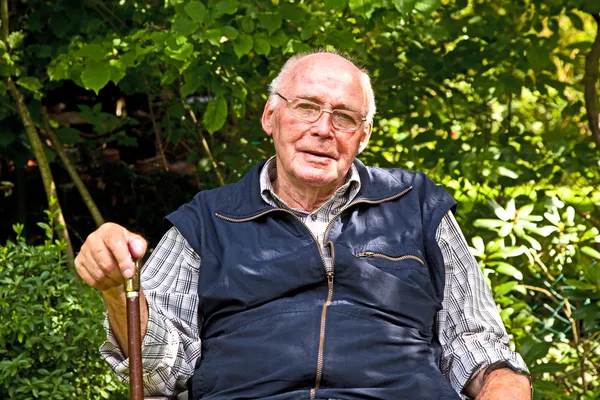 Portrait of elderly man sitting happy in his garden — Stock Photo, Image