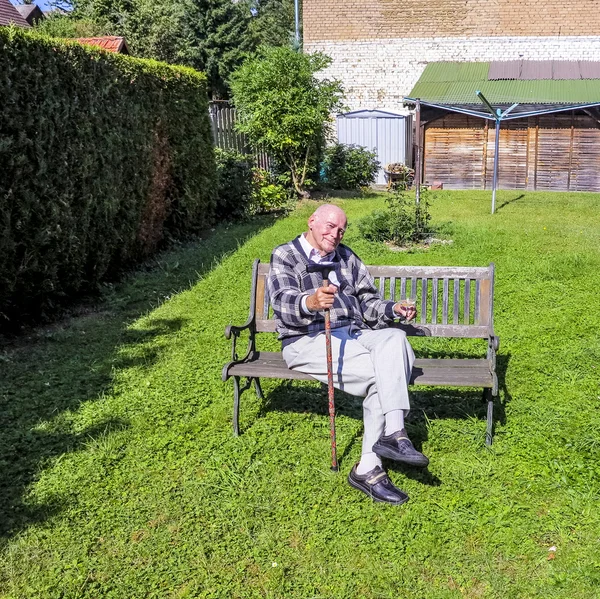 Onun bahçesinde bir bankta oturan yaşlı adam sahiptir — Stok fotoğraf