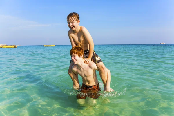 Fratelli stanno godendo la limpida acqua calda nell'oceano e giocare Foto Stock