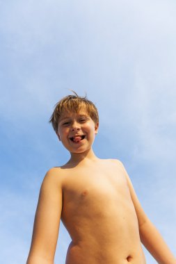 mutlu gülümseyen genç oğlan mavi gökyüzünün altında sahilde poz