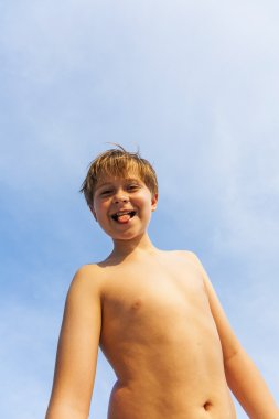 mutlu gülümseyen genç oğlan mavi gökyüzünün altında sahilde poz