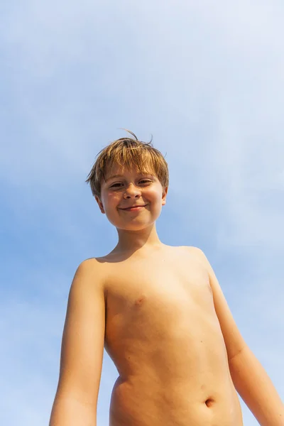 Glada leende ung pojke poserar på stranden under blå himmel — Stockfoto