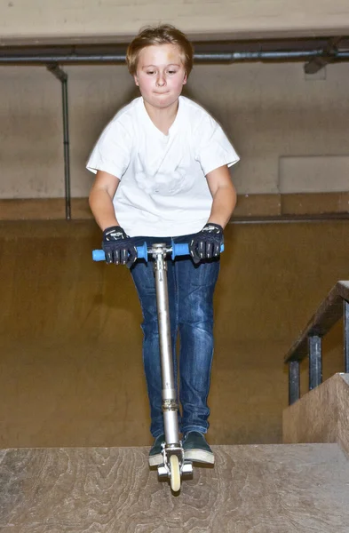 El chico va a patinar con su scooter en un salón interior. — Foto de Stock