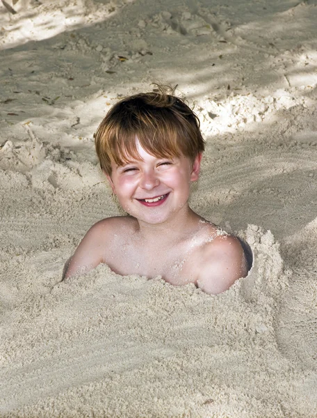 Heureux jeune garçon couvert de sable fin à la plage — Photo