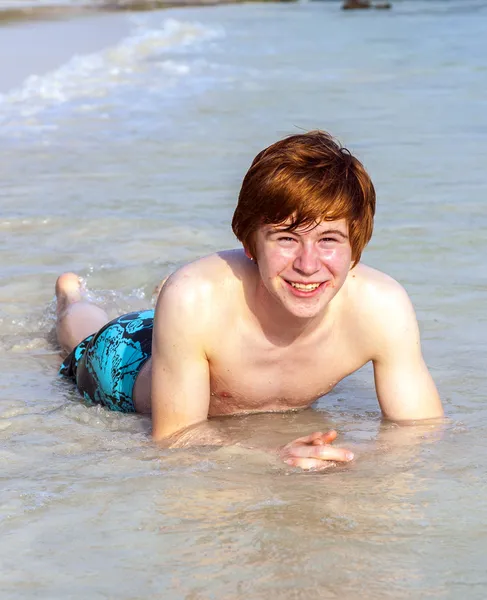 Boy enjoys lying in the spume of the tropical beach Stock Photo