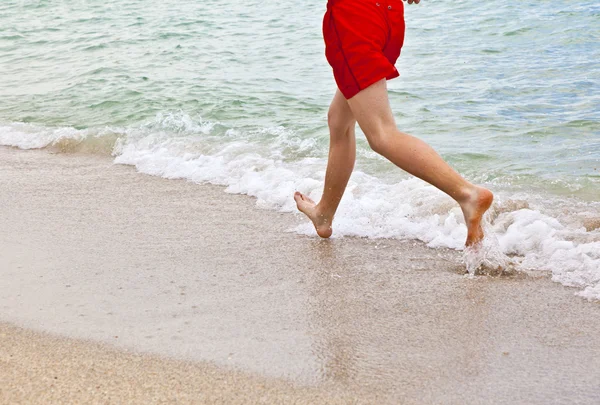 Fötter av pojke löper längs stranden — Stockfoto