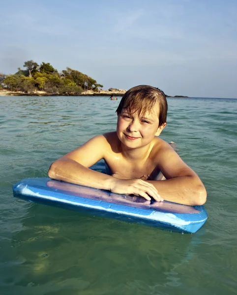 Boy is swimming on his surfboard and happily smiling in a beaut — Stock Photo, Image