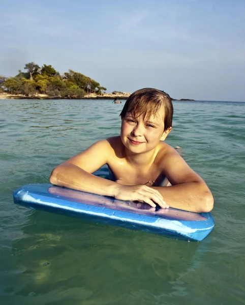 Garçon nage sur sa planche de surf et sourit joyeusement dans un beaut — Photo