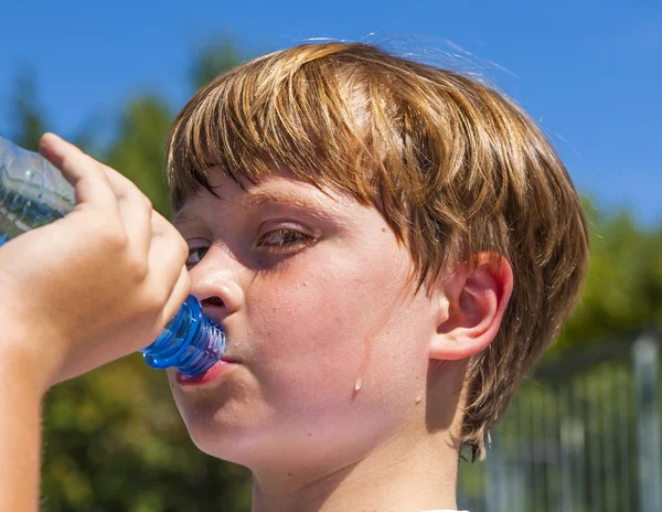 Young boy drinks water out of a bottle — Stock Photo, Image