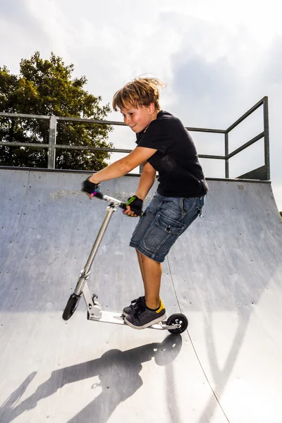 Chico disfruta saltando con su scooter en el medio tubo —  Fotos de Stock