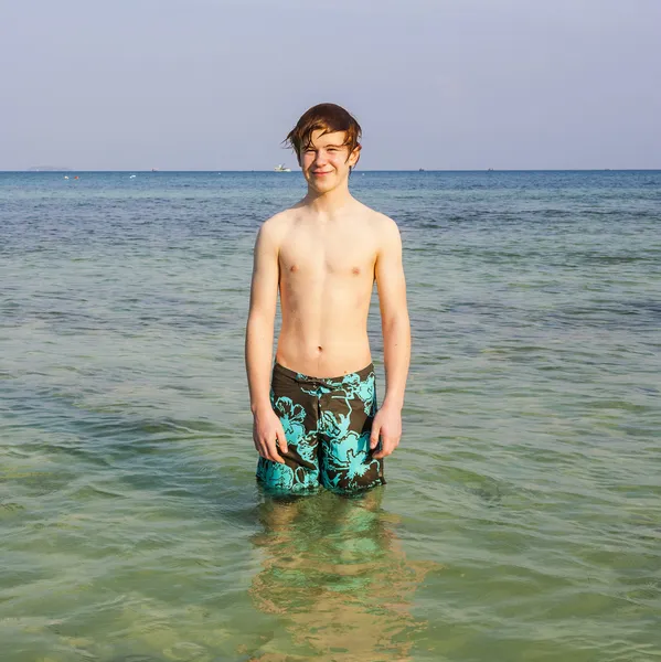 Young boy is standing in the beautiful clear sea and enjoys the — Stock Photo, Image